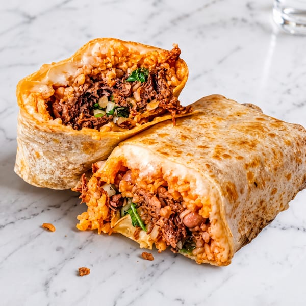 A large burrito, cut in half, revealing a filling of rice, beans, and shredded meat on a marble surface.
