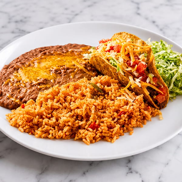 A plate of two crispy tacos with rice, refried beans, and shredded lettuce on a marble surface.