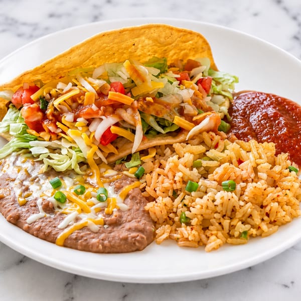 A hard-shell taco with lettuce, cheese, and salsa, served with refried beans, rice, and red sauce.